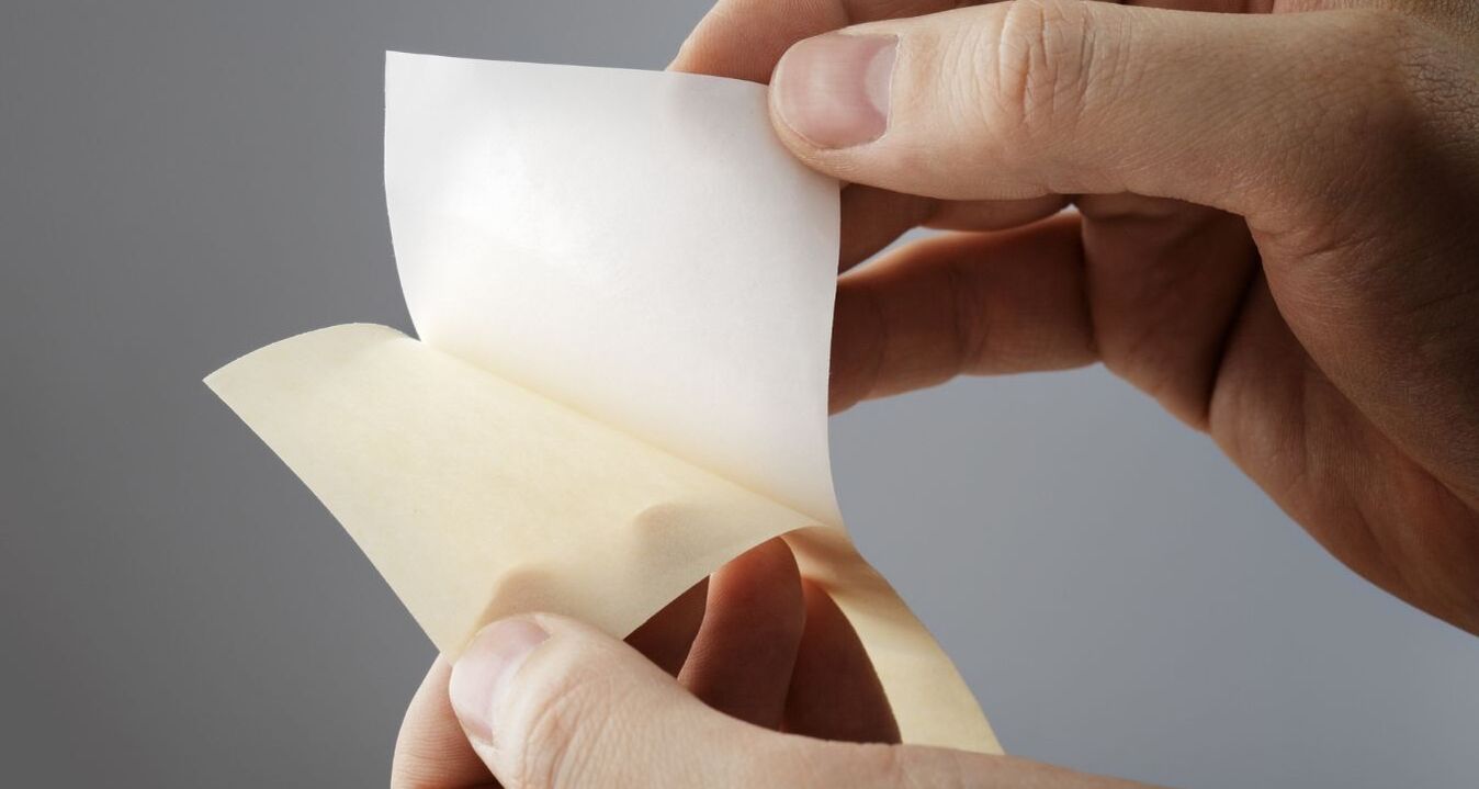 Le papier antiadhésif est retiré du support siliconé Une main détache un papier antiadhésif blanc d'un support siliconé. Gros plan sur un papier antiadhésif enduit sur une face destiné aux applications industrielles, aux adhésifs, à la technologie des adhésifs et aux solutions d'emballage.