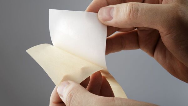 Le papier antiadhésif est détaché du support siliconé Une main détache un papier antiadhésif blanc d'un support siliconé. Gros plan sur un papier antiadhésif enduit sur une seule face destiné aux applications industrielles, aux adhésifs, à la technologie des adhésifs et aux solutions d'emballage.