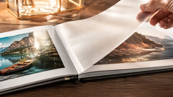 Album photo haut de gamme avec des intercalaires siliconés pour protéger les photos de grande qualité Album photo haut de gamme à couverture ouverte, avec des intercalaires transparents siliconés entre des photographies ultra-brillantes, posé sur une élégante table en bois baignée par la lumière chaude du jour – une solution de protection haut de gamme pour vos tirages photo et vos souvenirs.