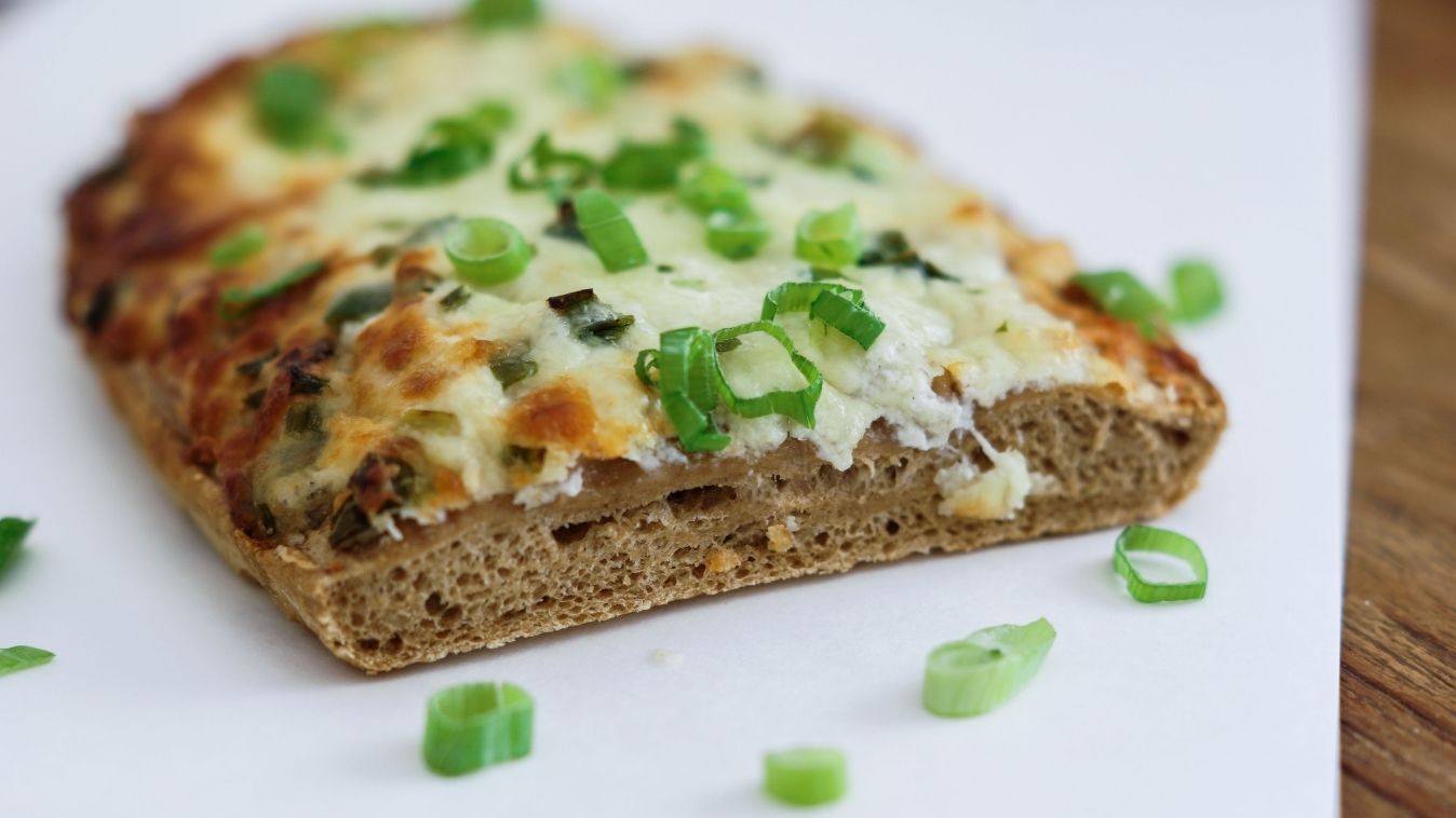 Carton de cuisson pour les processus de cuisson industriels. Parfait pour un minimum d'effort et des résultats parfaits. Pièce de boulangerie salée sur carton de cuisson Blechrein, garnie de fromage frais et d’oignons verts.